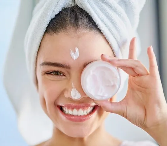 Woman smiling with a towel on her head, applying face cream